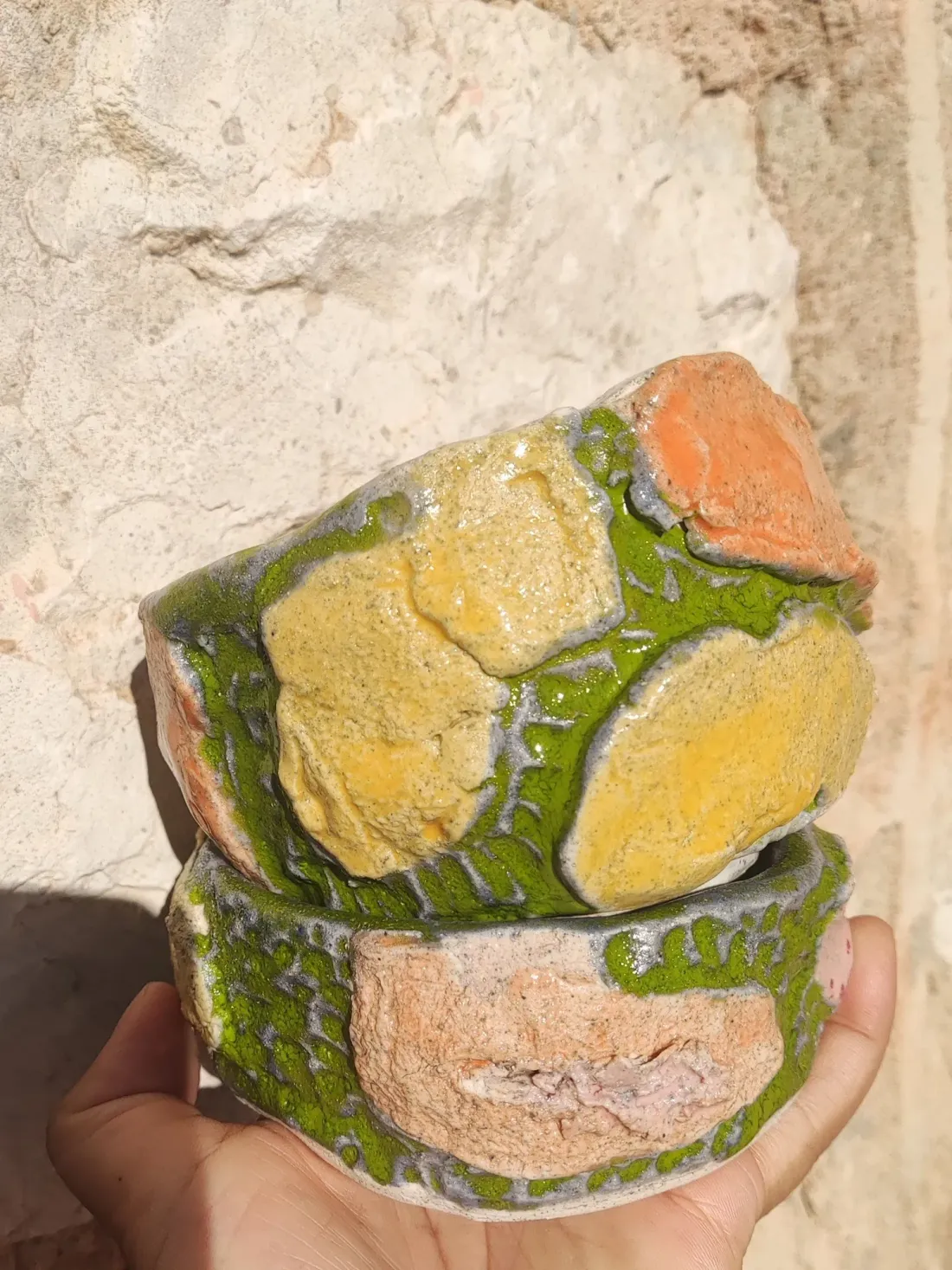 Green cup holding mandarins, against a stone wall