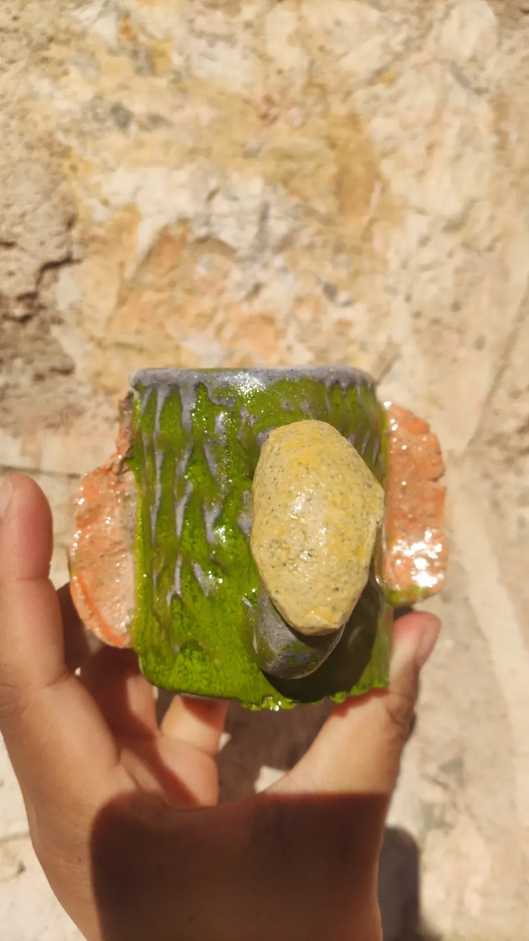 Cup with dripping green glaze, against stone